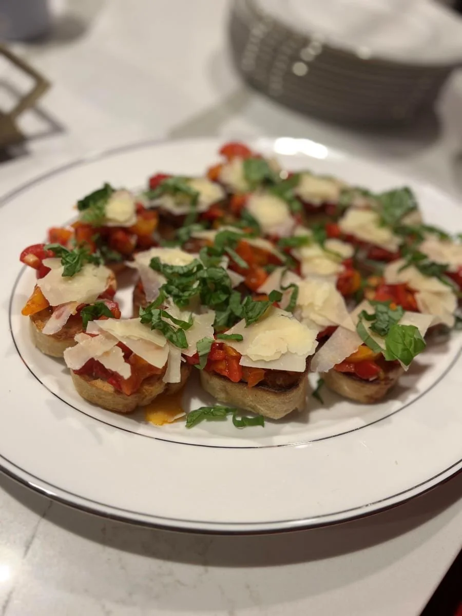 Plate of bruschetta topped with chopped tomatoes, basil, shaved Parmesan cheese, and other toppings.