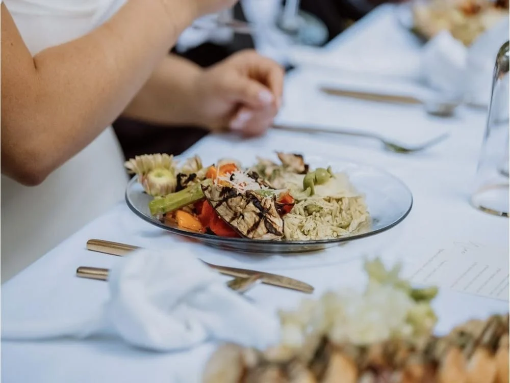 A plate of grilled vegetables, including eggplant, peppers, and celery, on a white tablecloth at a dining event.