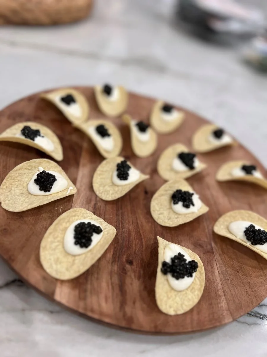 Tortilla chips topped with cream cheese and black caviar, arranged on a wooden serving board.