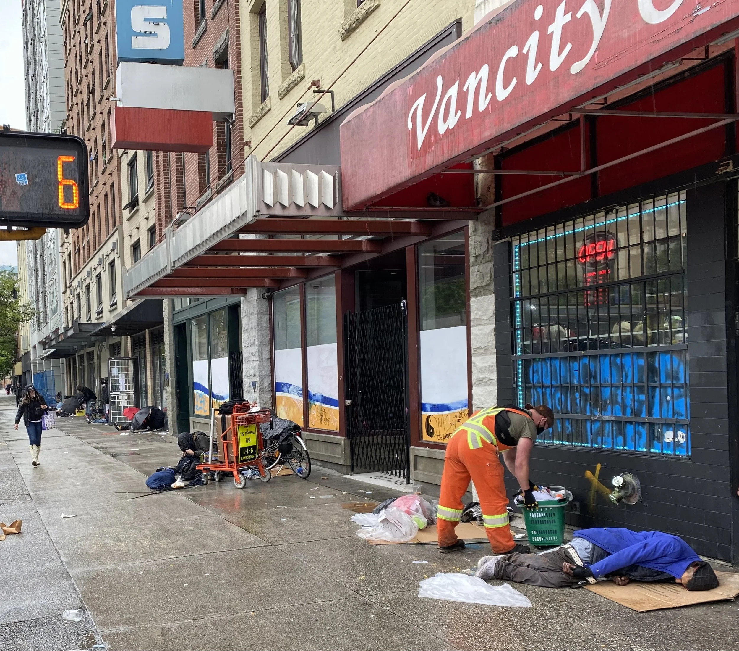 Vancouver Downtown Eastside scene with homeless person sleeping on sidewalk in front of convenience store.
