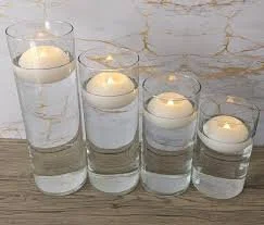 Four clear glass vases with lit floating candles on a wooden surface.