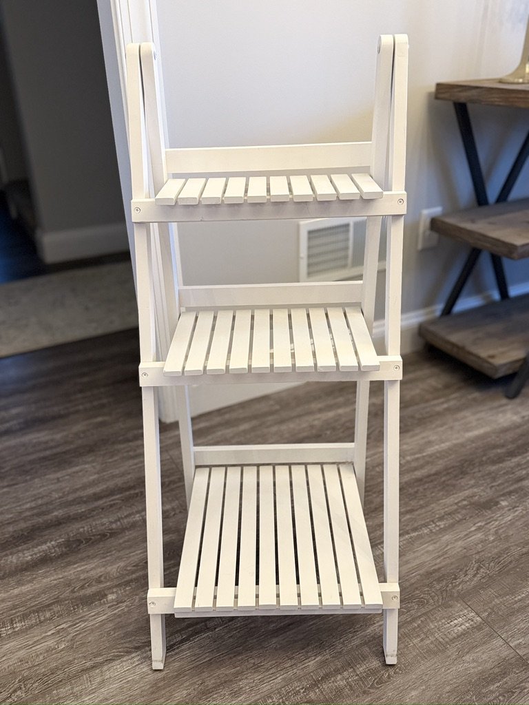 White wooden three-tiered shelf on a wooden floor in a room.