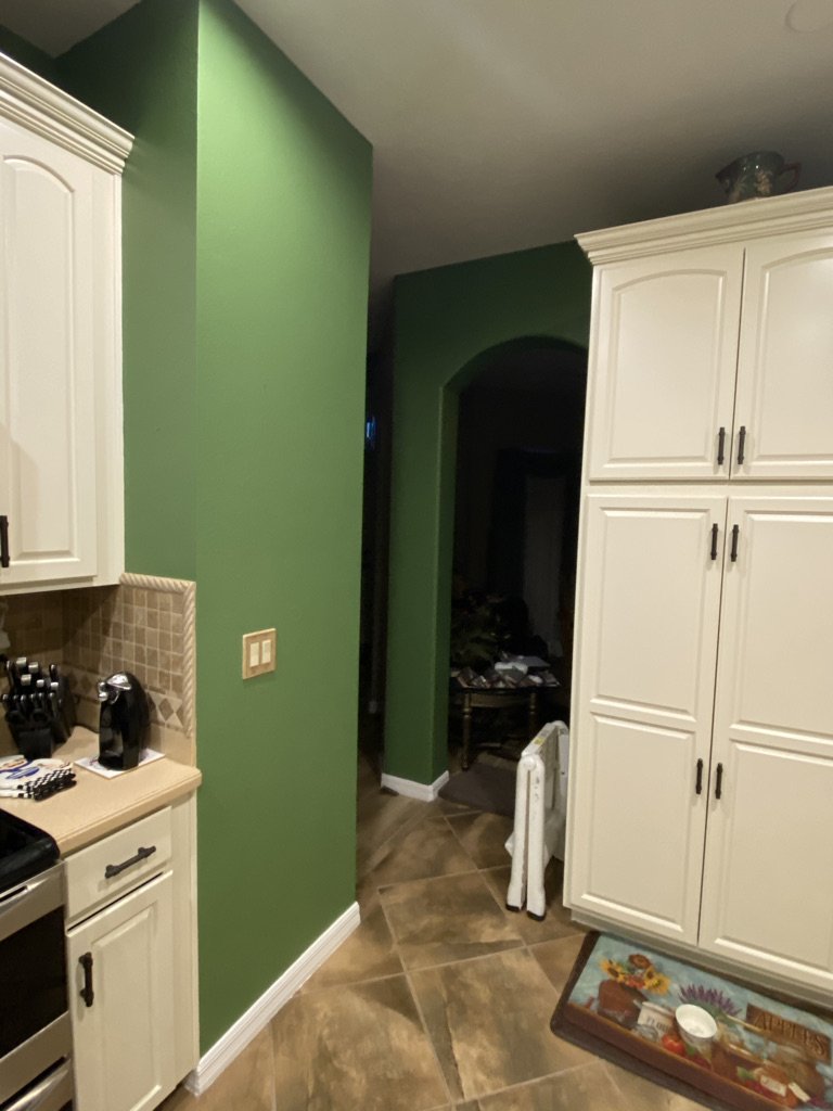 Kitchen corner with green wall, white cabinets, and tiled floor.