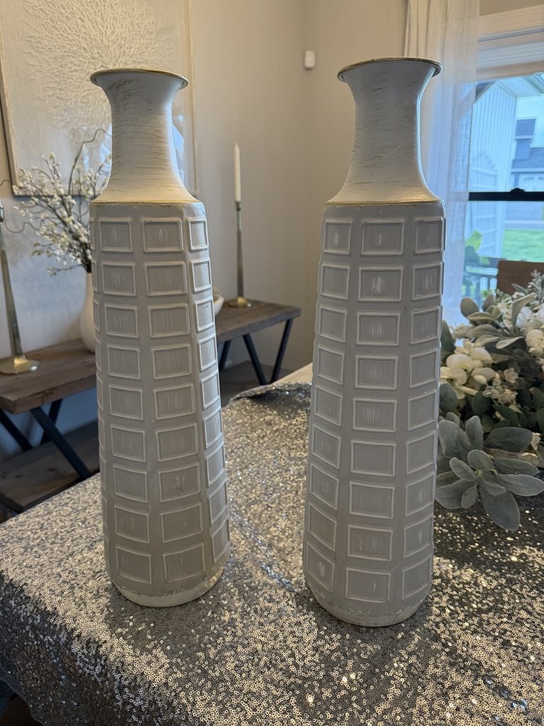Two tall decorative vases with textured square patterns on a glittery tablecloth.