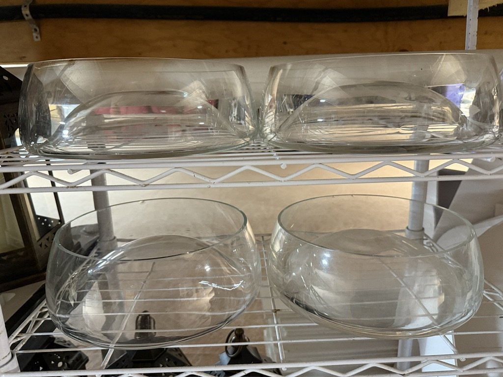 Four large glass bowls on a white metal shelf.