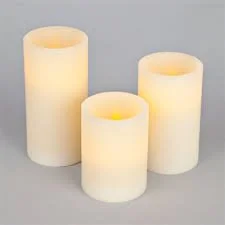 Three lit pillar candles of varying heights on a gray background.