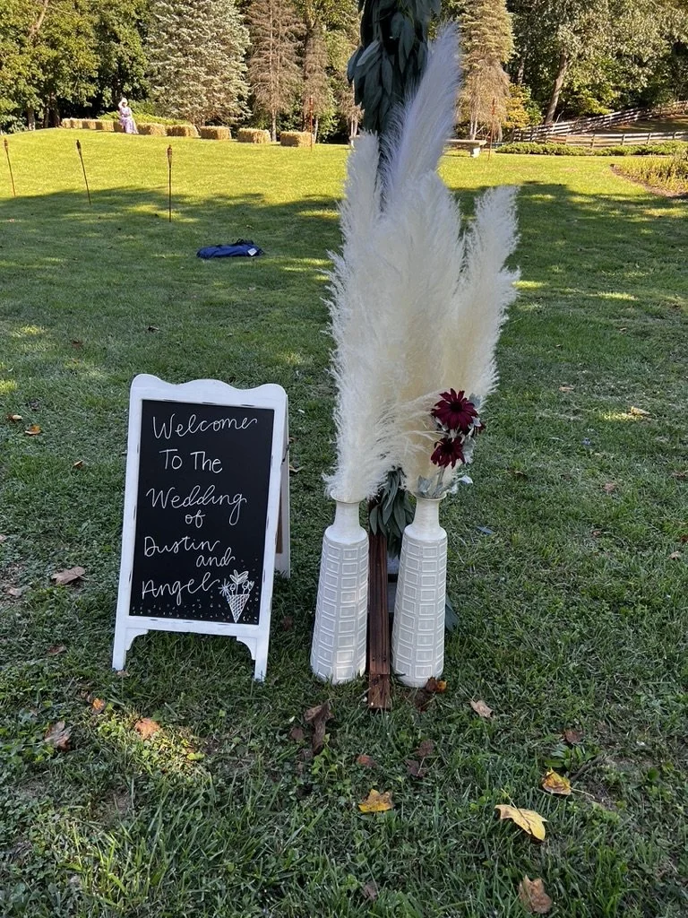 Outdoor wedding sign with white vases and pampas grass on grass field