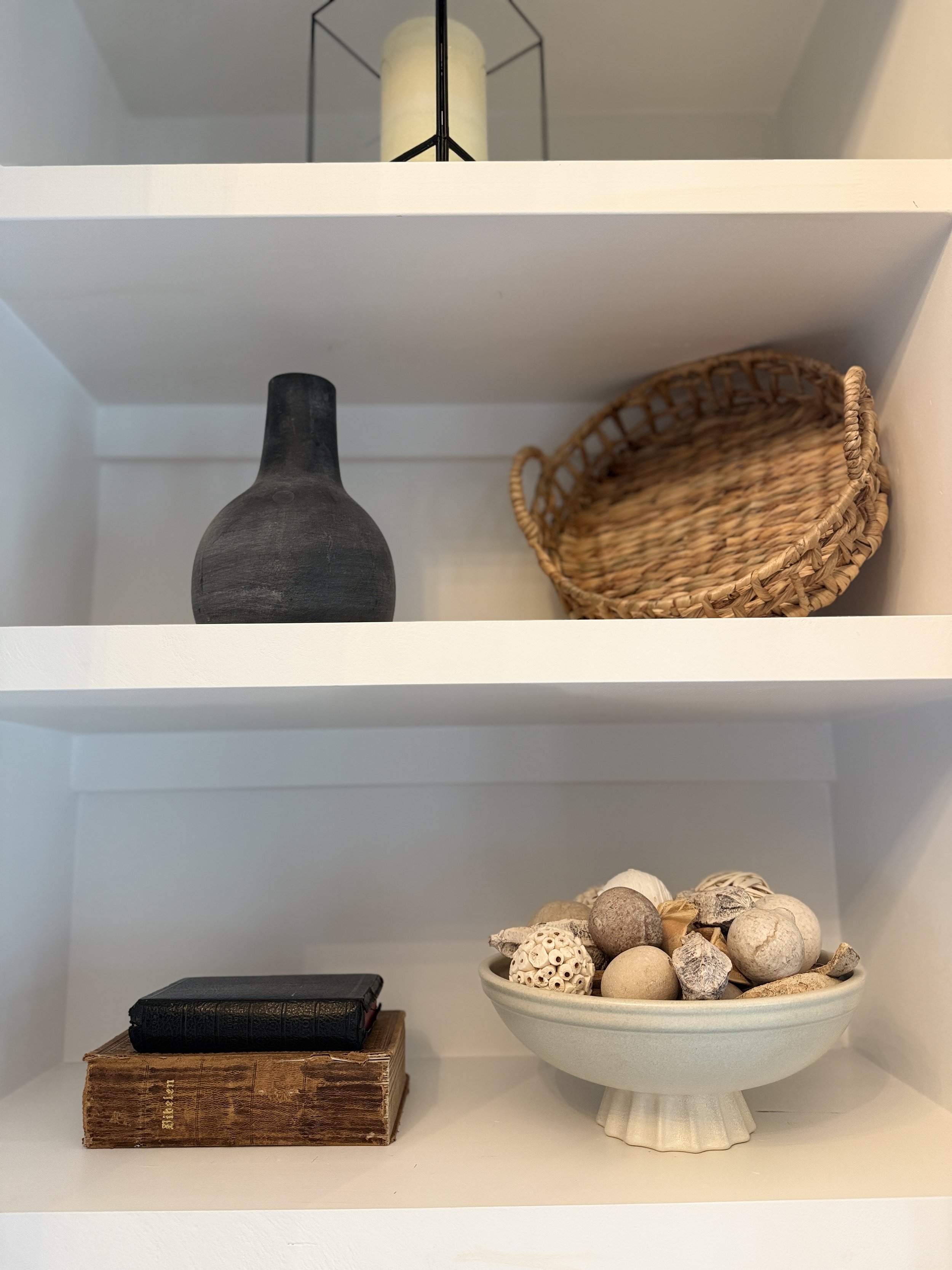 Decorative shelves with candle holder, black vase, wicker basket, old books, and bowl of natural objects