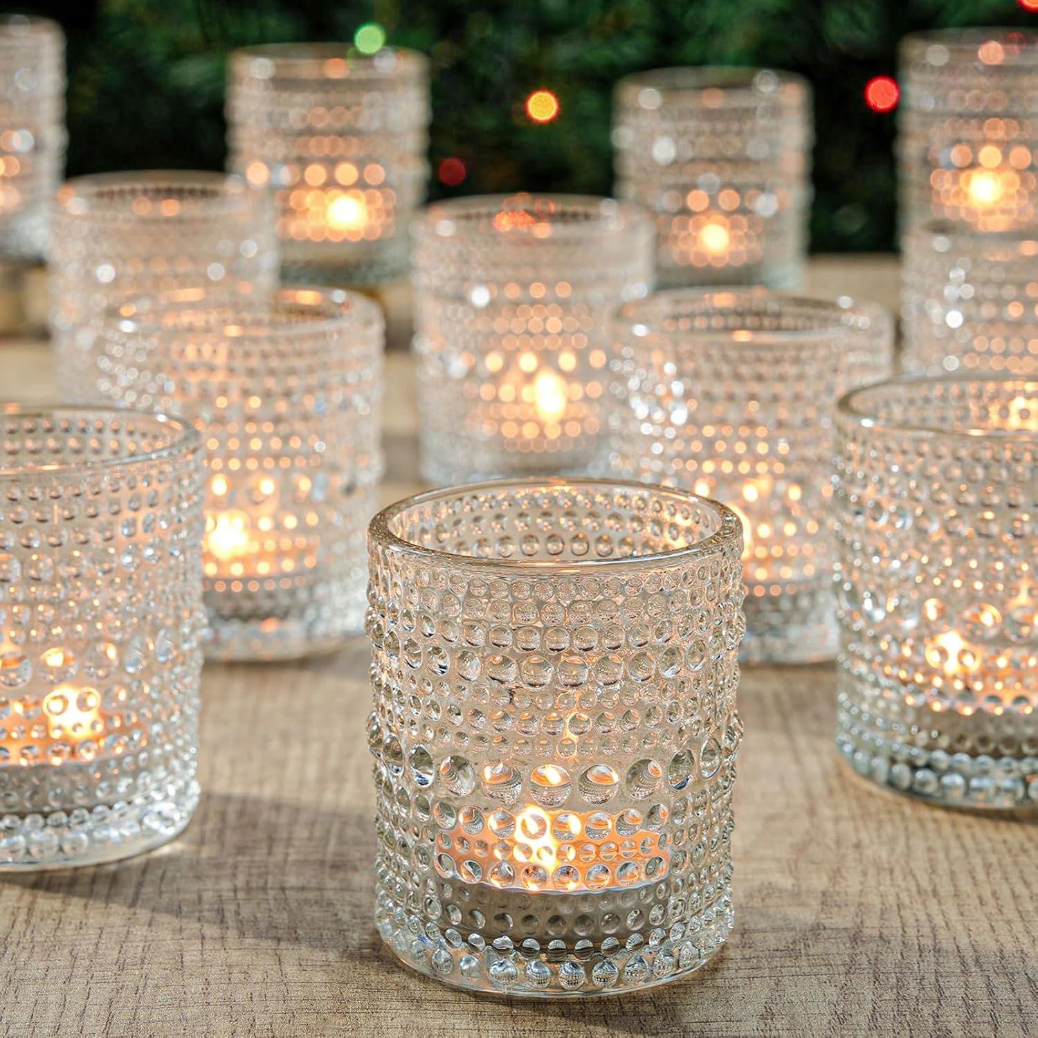 Multiple glass candle holders with dotted pattern containing lit tealight candles on a wooden surface.