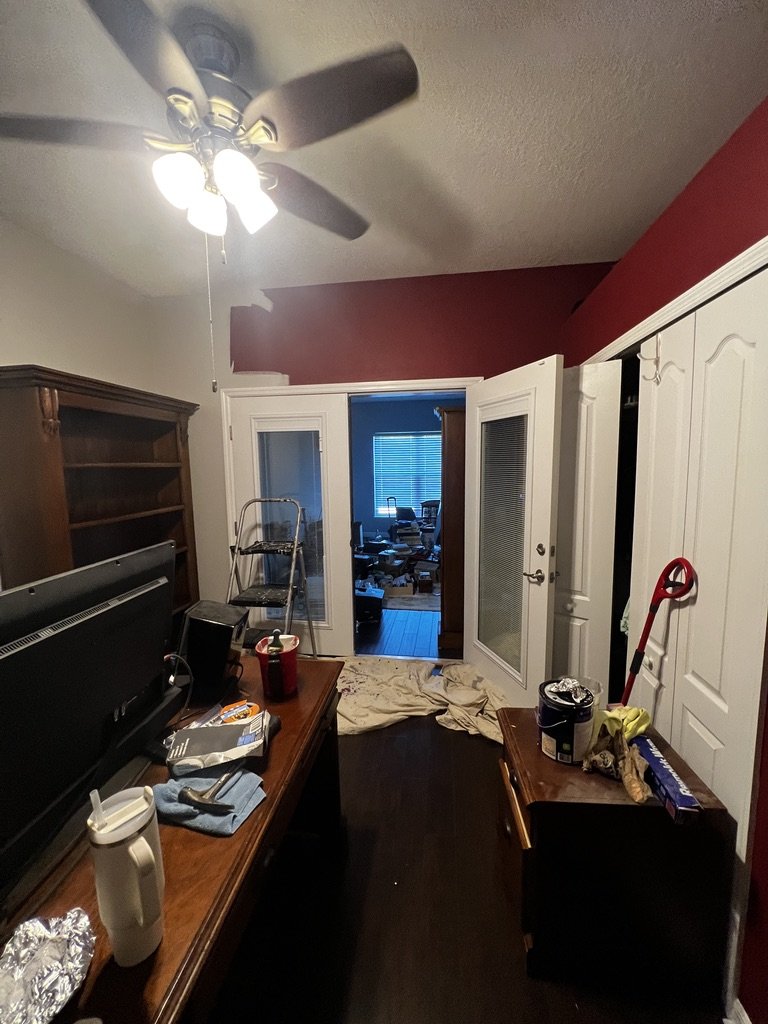 Room in disarray with repainting supplies, ladder, bookshelves, and furniture.