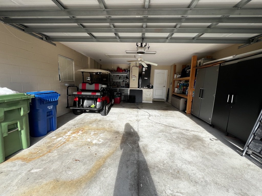 Interior of a residential garage featuring a golf cart, storage cabinets, shelves, green and blue recycling bins, and various tools.