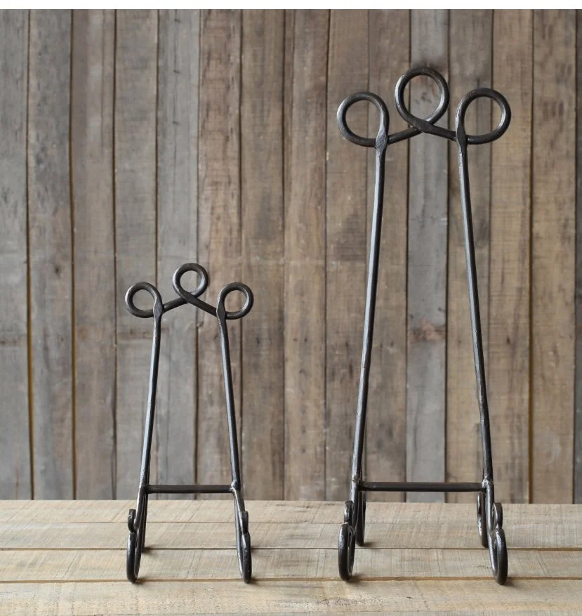Two metal easels of different sizes on a wooden surface with a wooden wall background.
