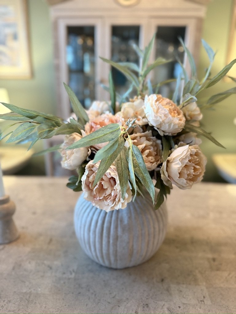A white ceramic vase with beige peonies and green leaves on a marble surface.