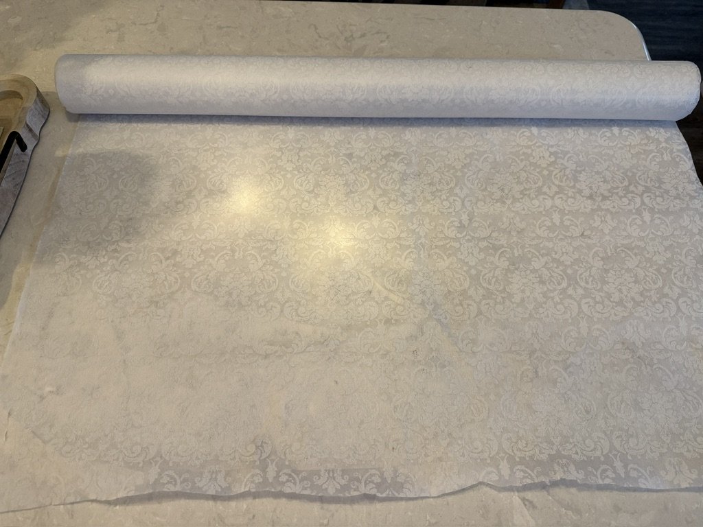 A roll of wallpaper with a subtle floral pattern unrolled partially on a table.
