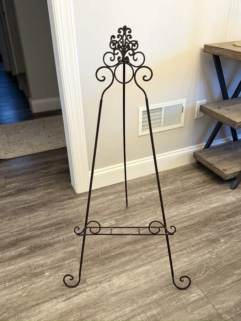 Decorative metal easel on wooden floor in a room corner.