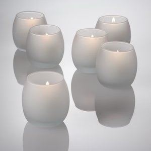 Six lit white candles in round holders on a reflective surface.
