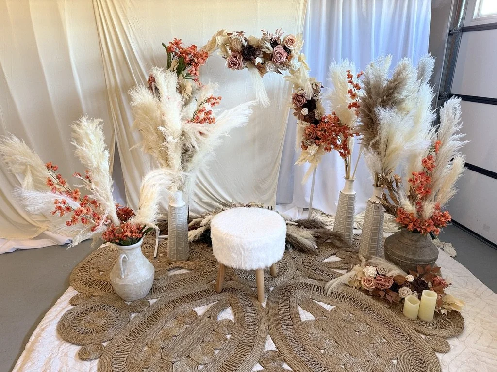 Bohemian floral arrangement with pampas grass and orange flowers surrounding a stool on a decorative rug.