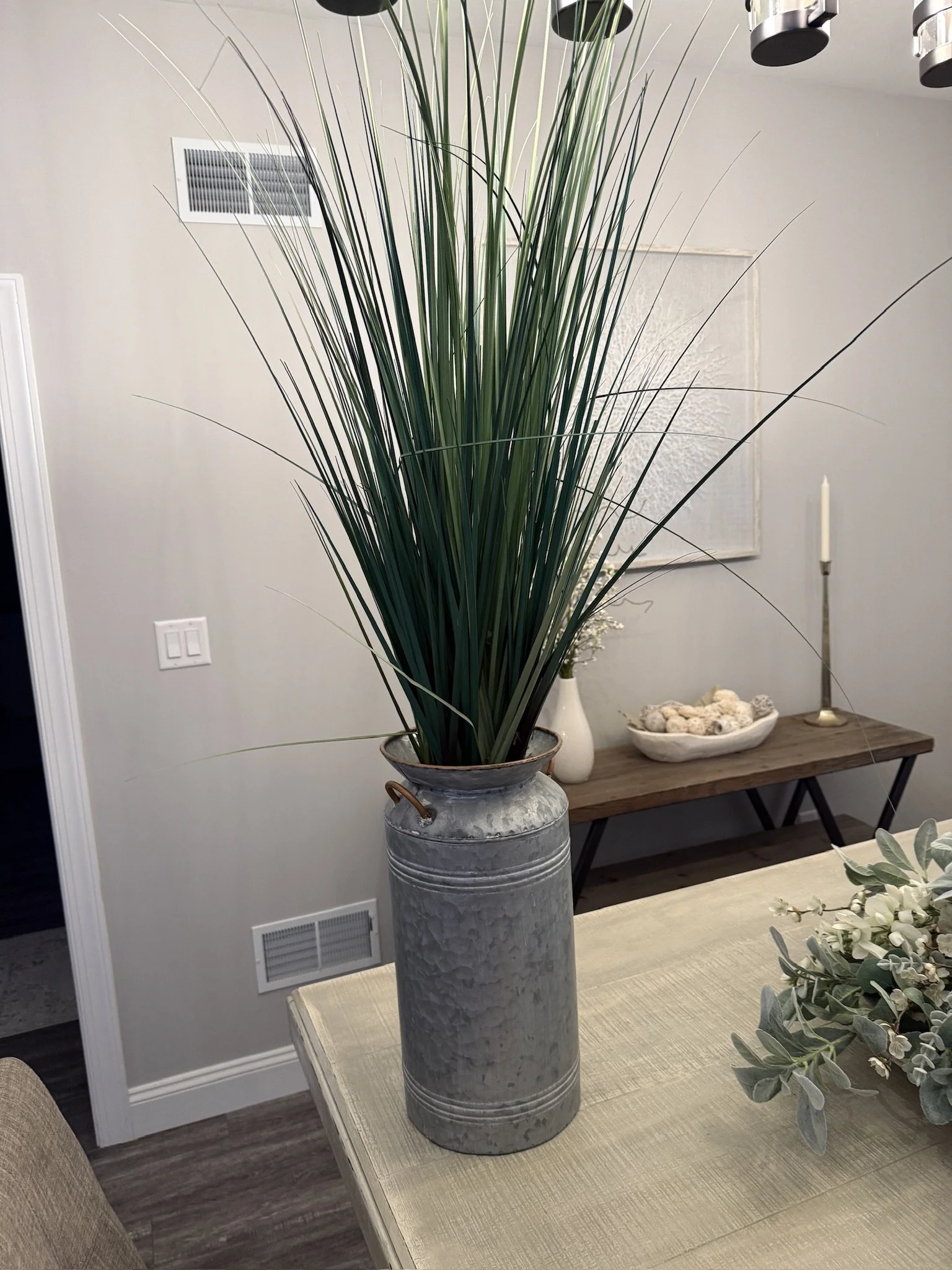 Decorative tall grass in a metal vase on a table in a modern living space.