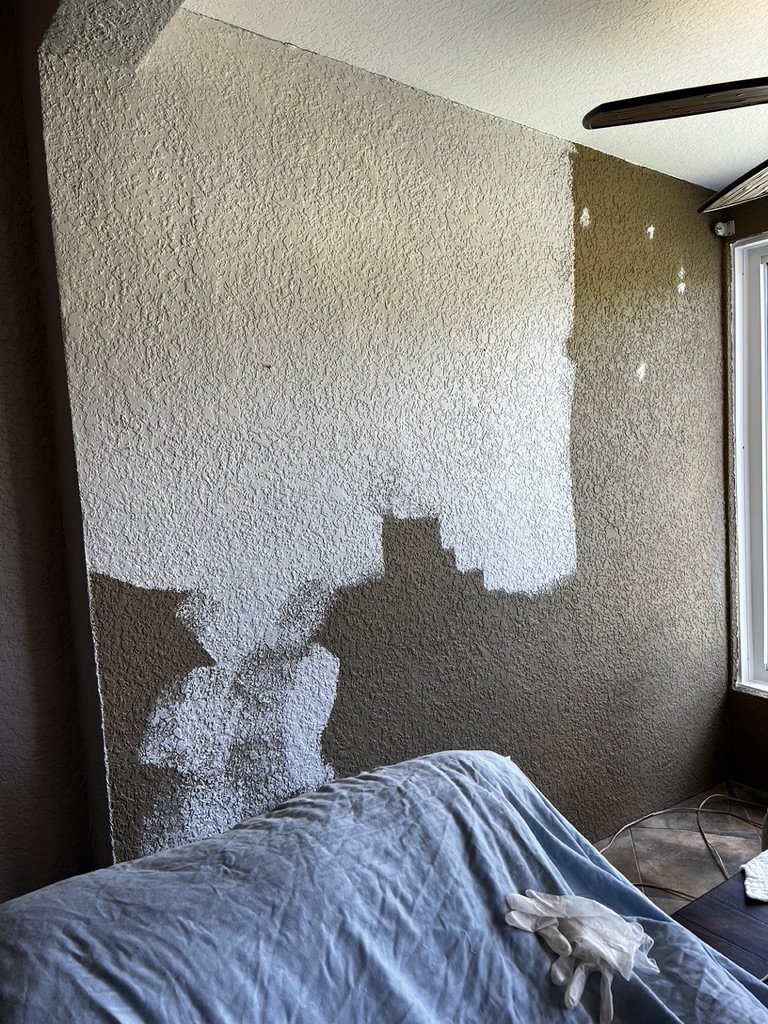 Partially painted wall with visible paint roller marks, covered furniture, and painting supplies.