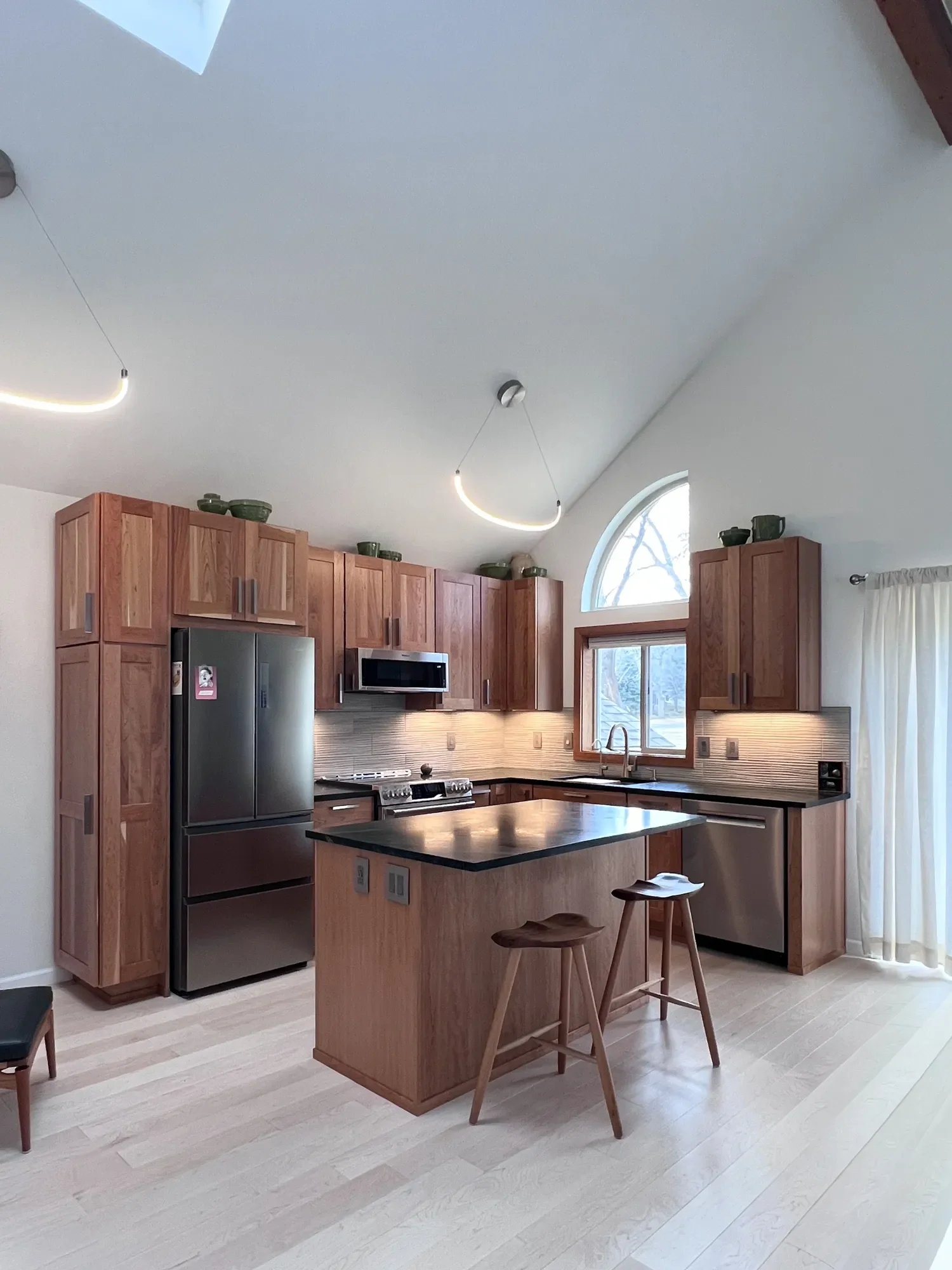 Overview of contemporary craftsman kitchen remodel in Newlands, Boulder, CO showcasing a newly reconfigured open layout, vaulted skylight ceilings, and kitchen island barstool seating between the kitchen and living areas