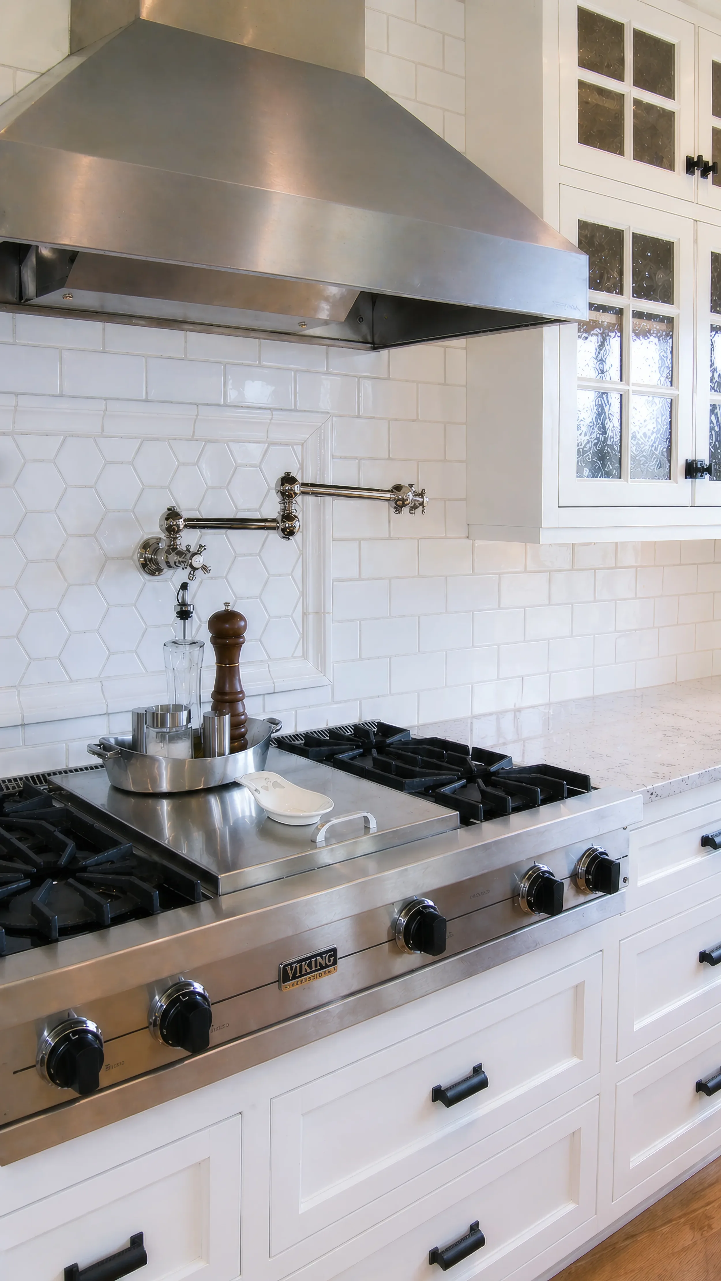 Detail view of stainless steel gas stove range complete with high end steel range hood, white subway tile backsplash with hexagon tile inset, and pot filler in Mapleton Hill, Boulder CO farmhouse kitchen remodel