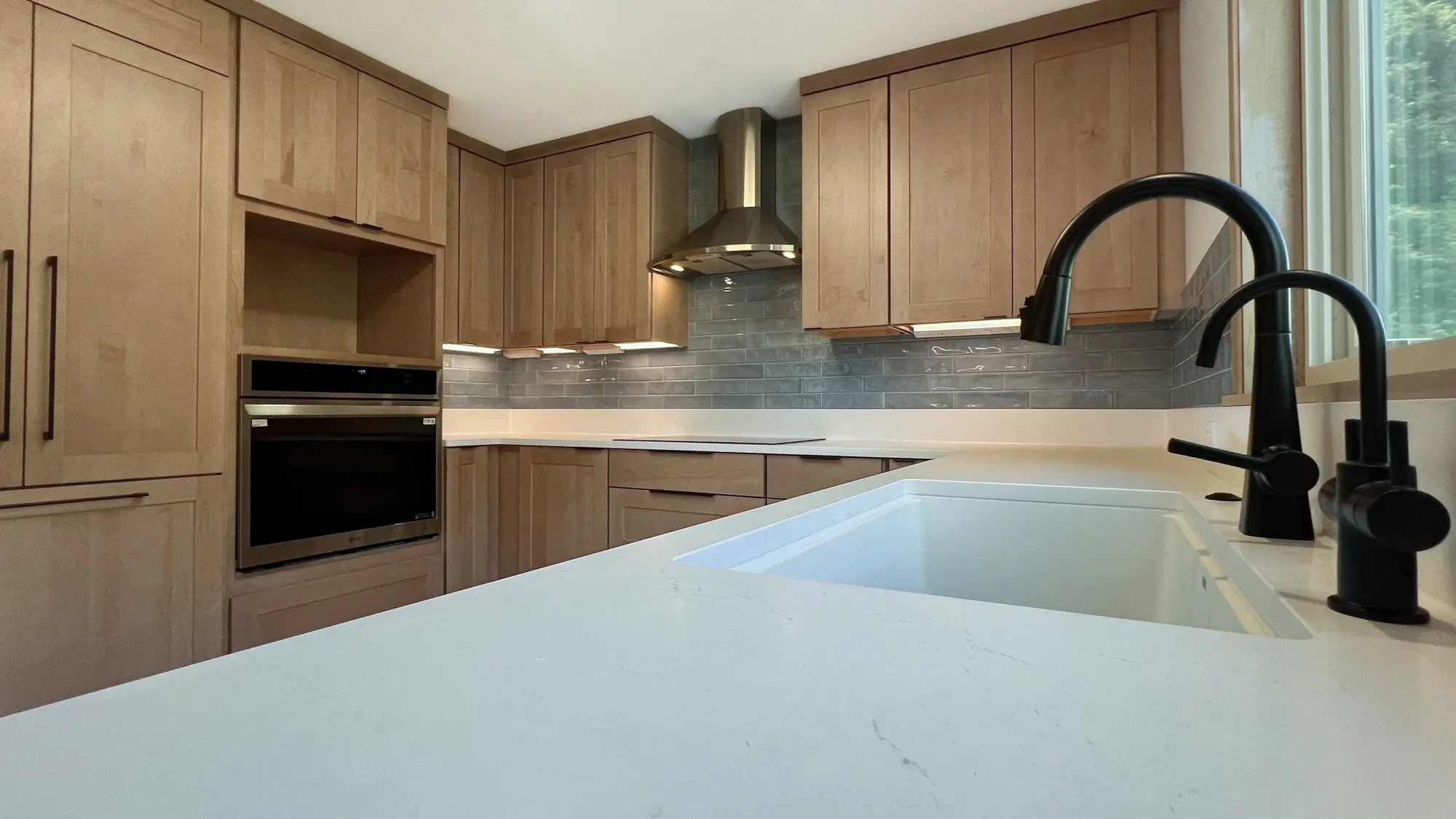 Newly remodeled contemporary craftsman kitchen in North Boulder, CO featuring custom oak cabinetry with hidden appliance panels, undercabinet LED lighting, and a white quartz countertop with black sink fixtures