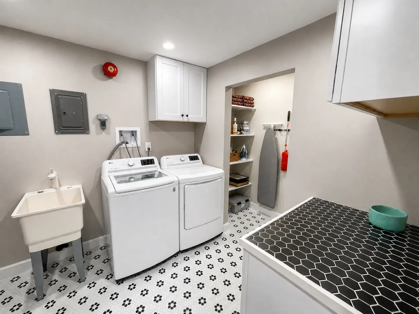 Renovated laundry room, part of a full unfinished basement remodel in Seven Hills, Boulder, CO, featuring hexagon tiled floors and countertop, white shaker cabinet storage, utility sink, and open doorway to closet storage with built-in shelving