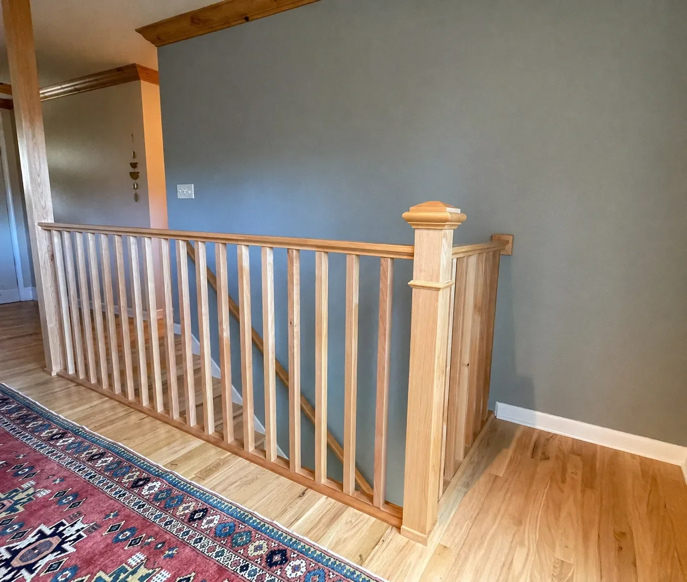 Interior view of a wooden stair railing and banister with hardwood flooring and a decorative area rug.