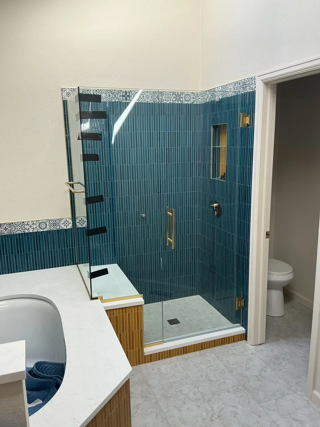 Newly installed custom cut shower glass on a blue tiled frameless walk-in shower, part of a high-end bathroom remodel project by Downy Home Remodeling in Gunbarrel, CO