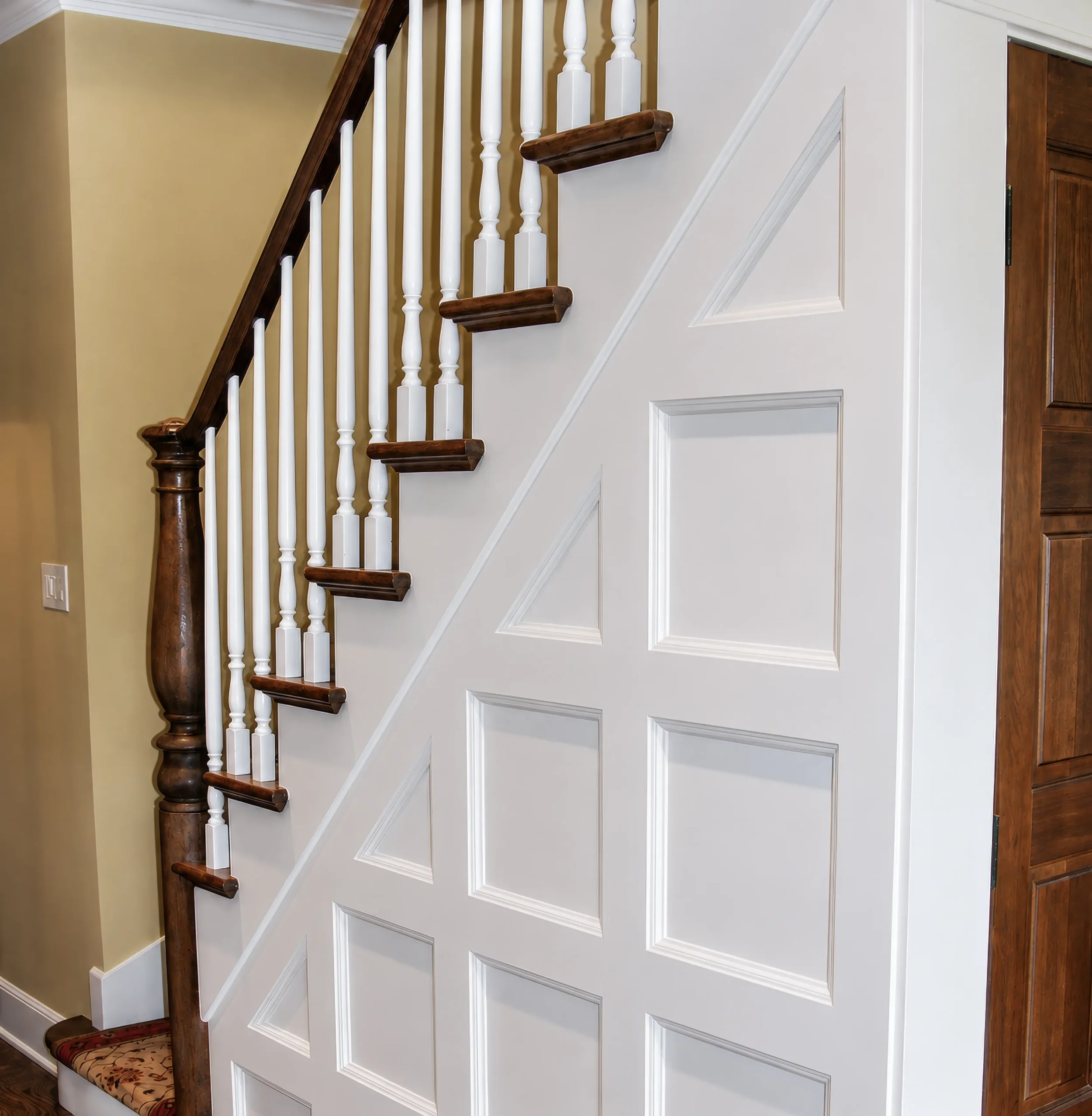 View of custom staircase with cherry hardwood flooring and banister, white square panel decorative wainscoting, and under stair pantry storage in Boulder, CO home remodel