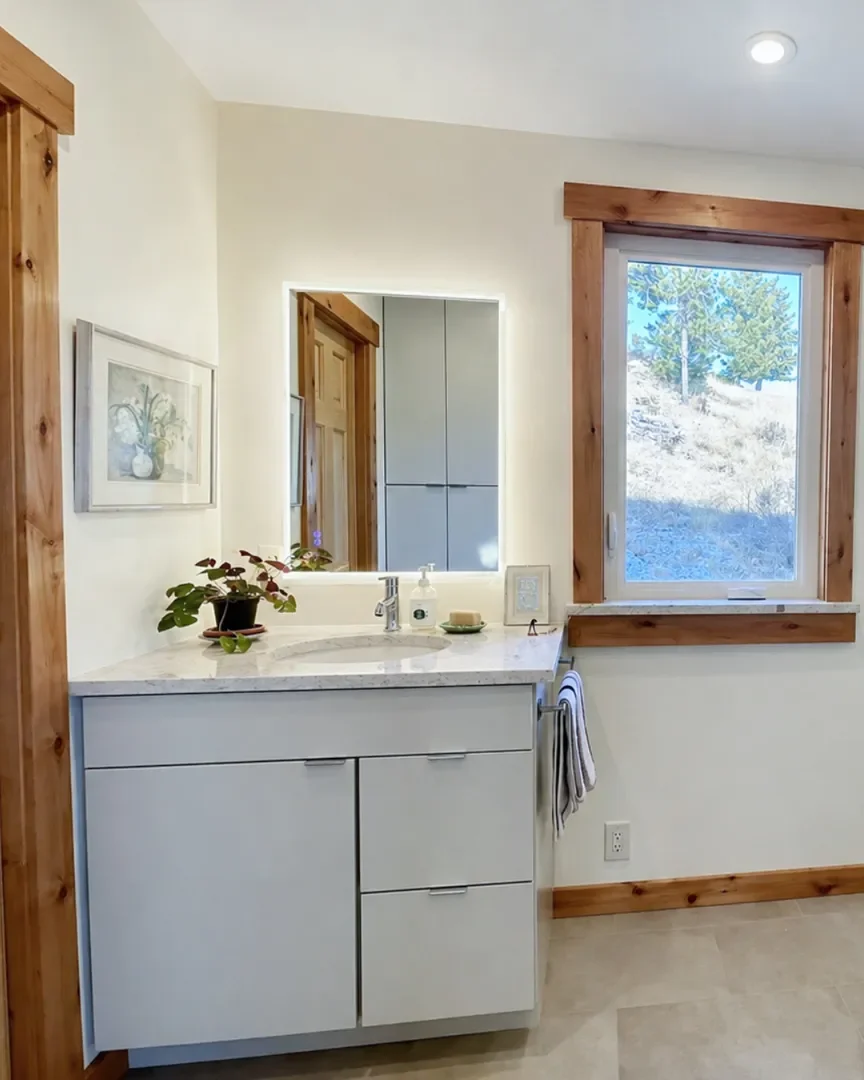 View of gray vanity with LED mirror reflecting matching closet cabinet storage, stone tile floors, and wood trim baseboards, door, and window in a Boulder, CO rustic mountain contemporary minimal bathroom remodel in Pine Brook Hills