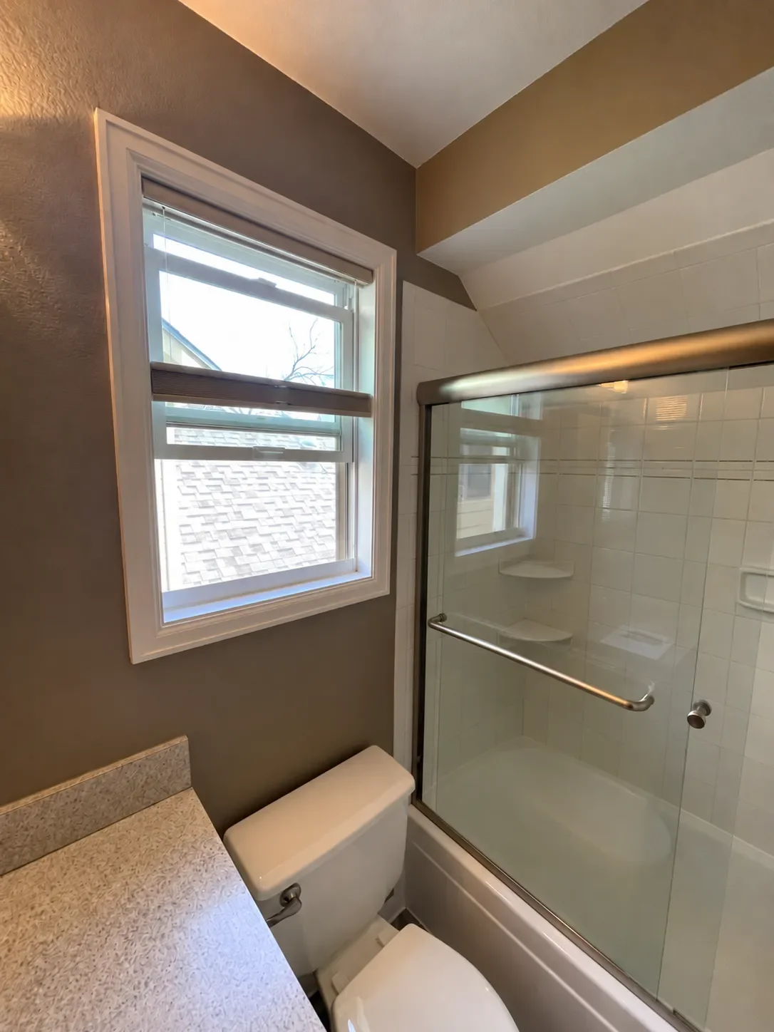 Bathroom in Noble Park, Boulder, CO before being remodeled by Downy Home Remodeling showing bathtub with sliding glass shower door frame, dark paint, and laminate vanity countertops.