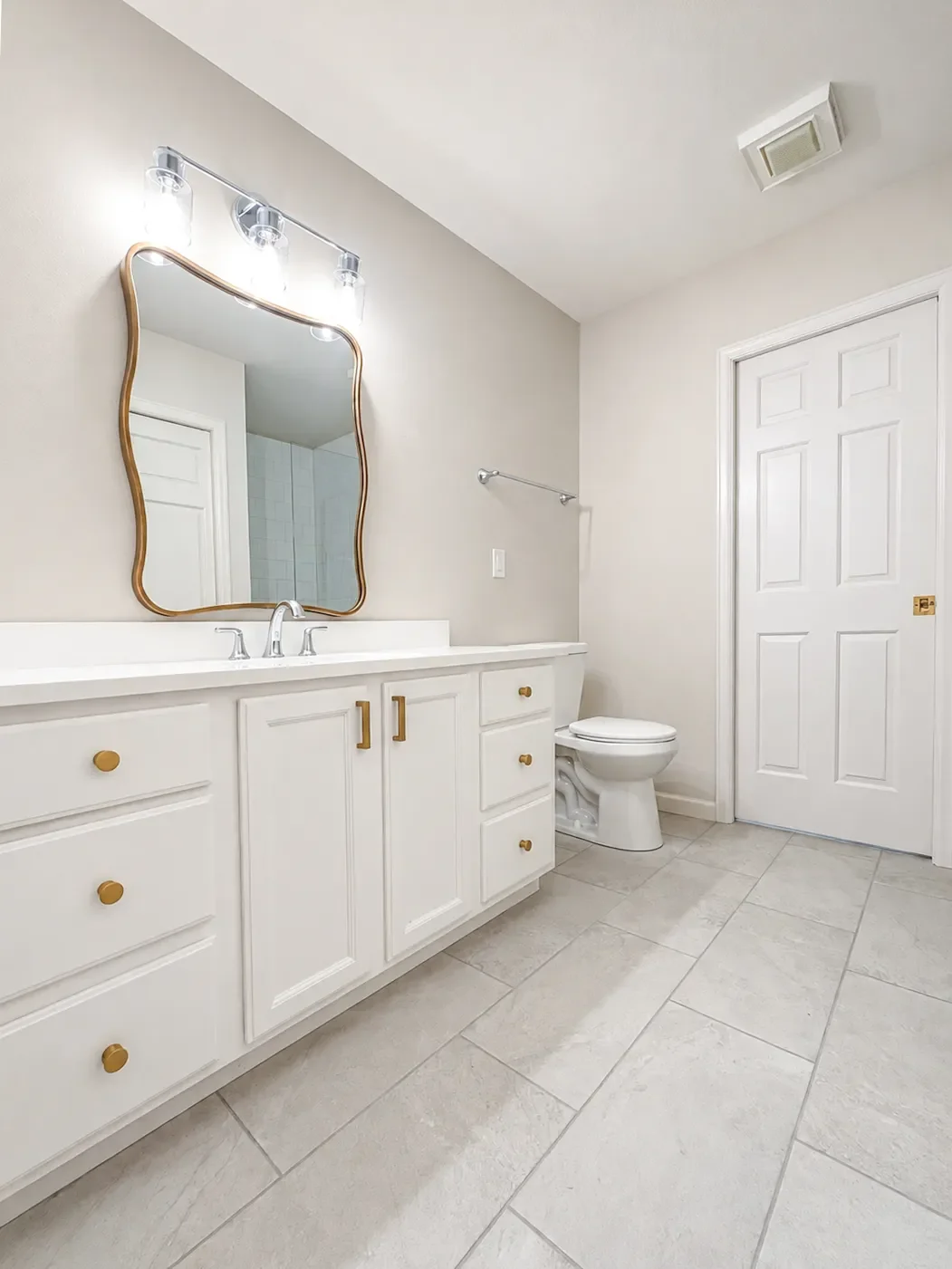 Minimal contemporary white guest bathroom, newly remodeled in Gunbarrel, CO, featuring a white shaker cabinet vanity with white quartz countertop, gold hardware, gold scalloped edge vanity mirror, and large panel light gray porcelain tile floor