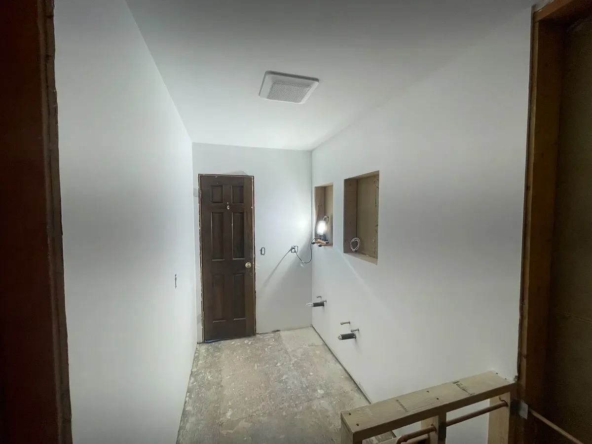 Fresh drywall smoothed to a level 5 finish in an unfinished Boulder, CO bathroom remodel, with recessed niches for future LED cabinet install, exposed subfloor, and frame for future walk-in shower with half wall partition