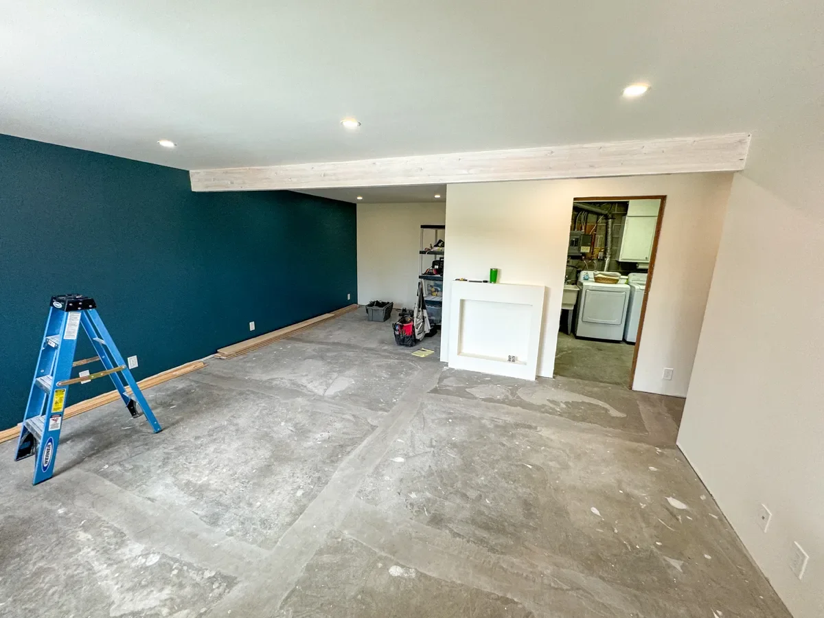 Boulder, CO basement remodel construction progress featuring unfinished concrete floors, freshly painted teal accent wall, and newly installed recessed can lighting