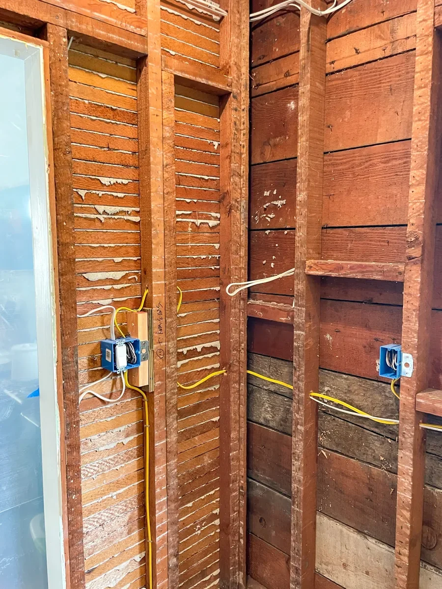 A Lafayette, CO kitchen remodel in progress showing interior wall with exposed wood studs and electrical wiring, including blue outlet boxes and yellow wires, and doorway sealed off with plastic painters sheeting
