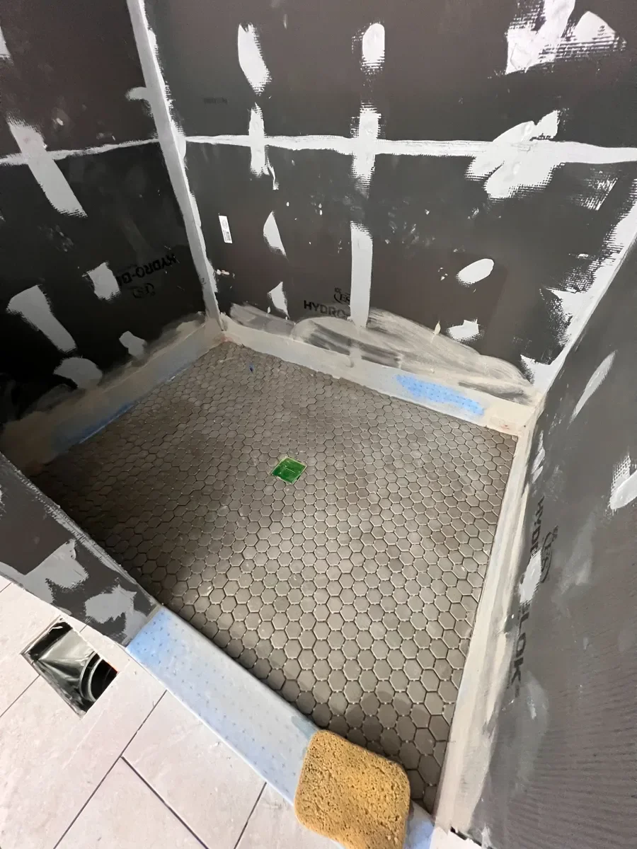 Boulder, CO bathroom remodel in progress featuring shower floor newly tiled with gray hexagon mosaic tile, and unfinished shower walls