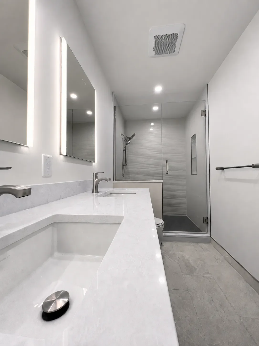 View along the long length of a quartz topped double vanity with two LED mirrors looking at the wavy tile walk-in shower against the far wall of the contemporary bathroom, newly remodeled in Boulder, CO- Table Mesa
