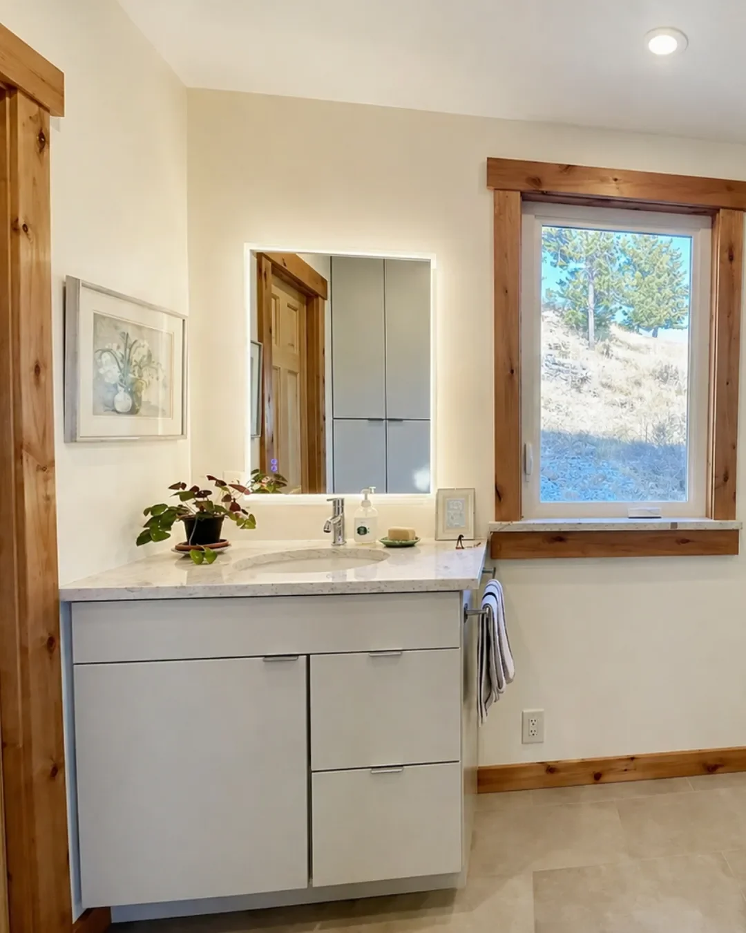 Remodeled primary bathroom in Pine Brook Hills, Boulder, CO with minimal gray euro style vanity, quartz countertop, heated stone tile floors, wood trim, built in linen storage, and LED mirror