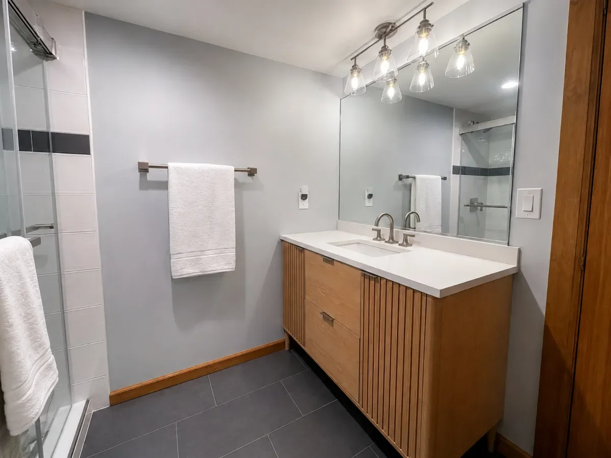Completed budget basement bathroom remodel in Niwot, CO featuring wooden vanity and walk-in shower, displayed next to a photo of the bathroom prior to remodeling.