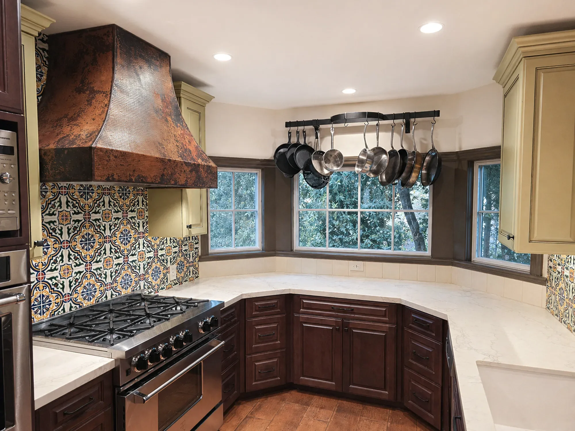 Louisville, CO remodeled mediterranean kitchen with bay window, white quartz countertops, yellow painted accent cabinets, spanish pattern tile backsplash, and copper stove range hood