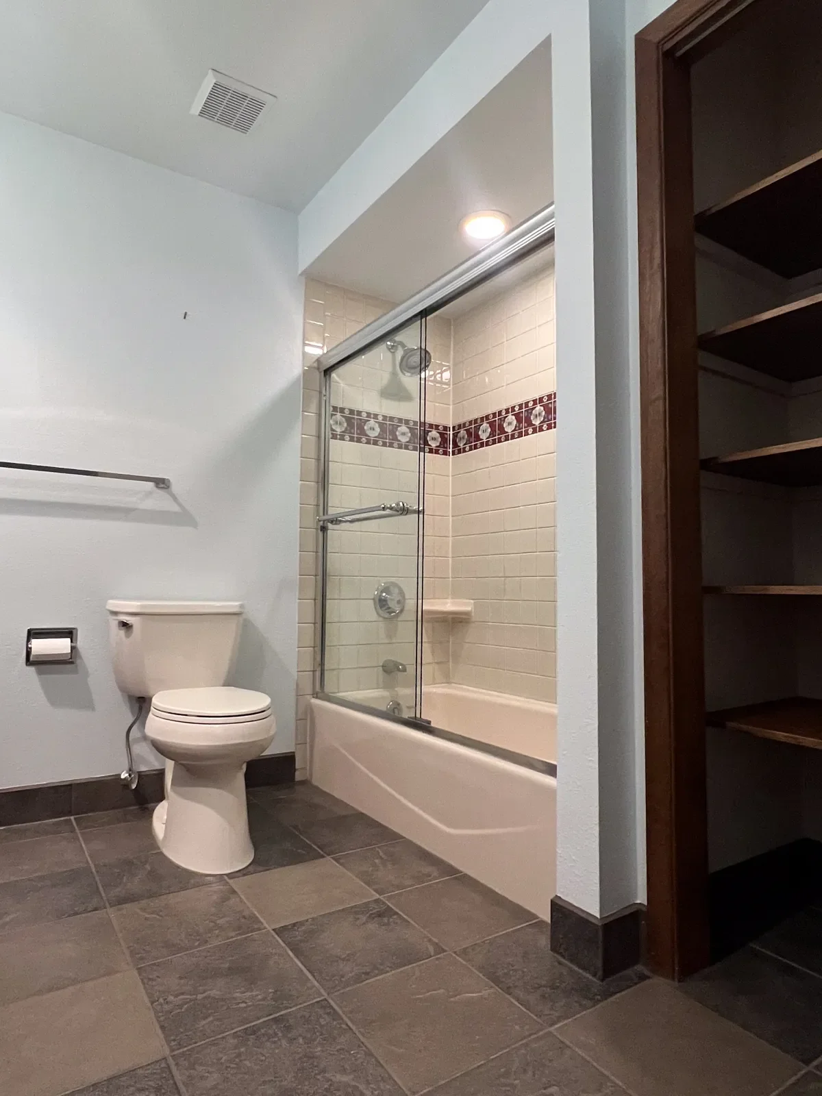 boulder, co vintage bathroom before remodel with dark stone tile floors, dark closet, and shallow bathtub with sliding glass framed shower