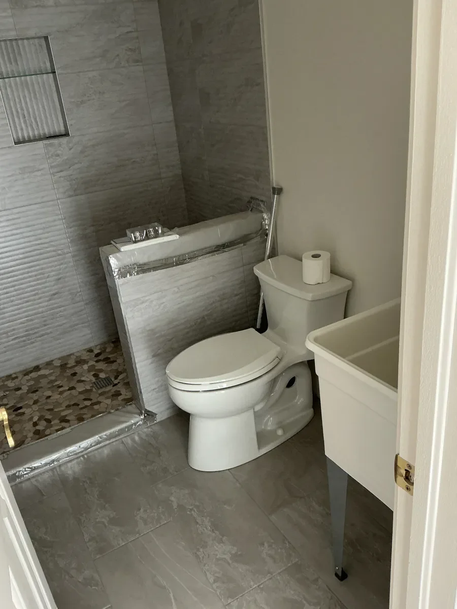 Unfinished Gunbarrel, CO guest bathroom remodel with newly installed toilet, fresh floor and shower tile, and a temporary utility sink in place of future vanity