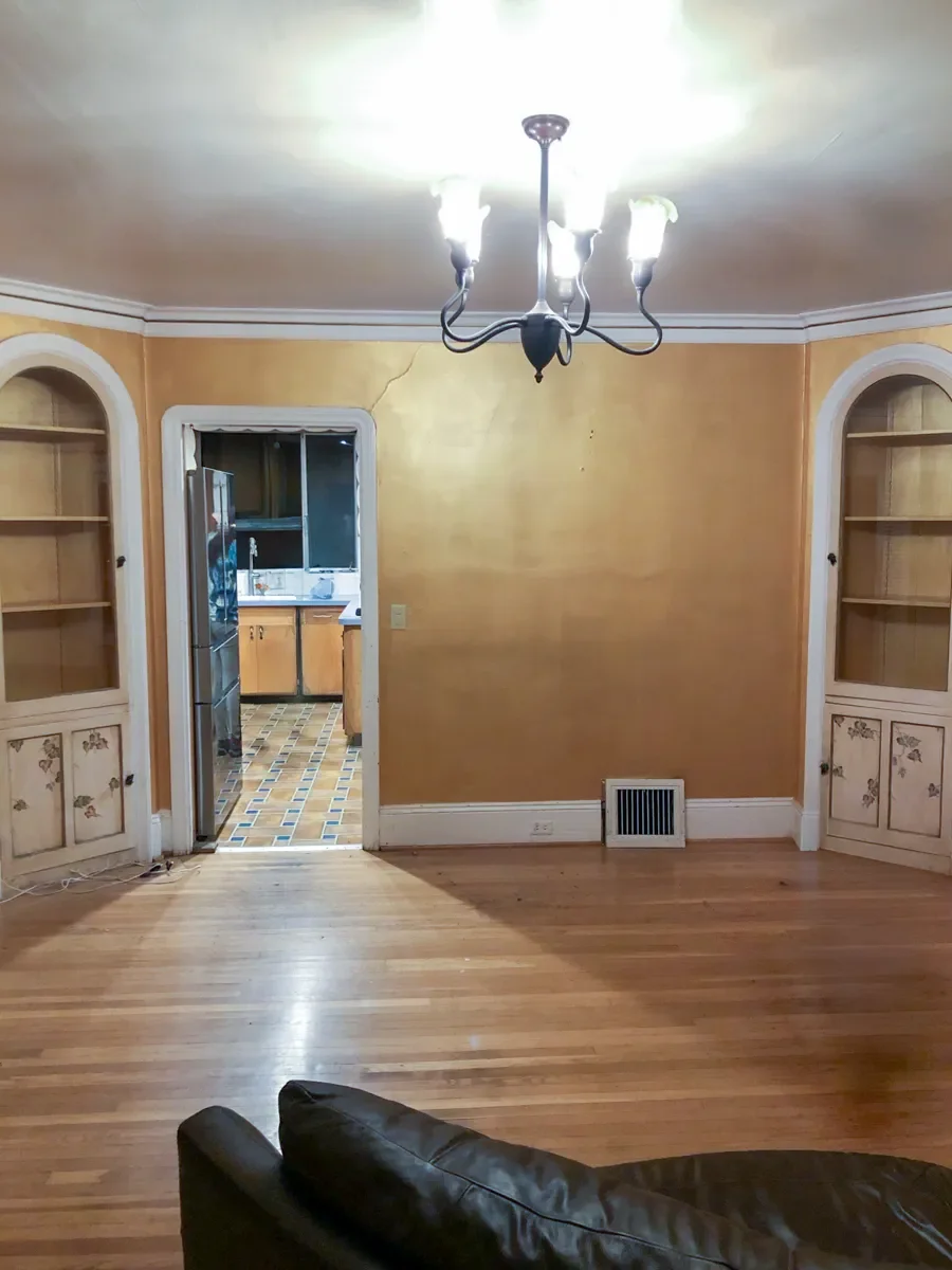 Empty living room before kitchen remodel floorplan redesign demo featuring water damaged mustard-yellow walls, hardwood floors, and built-in arched recessed hutch cabinets