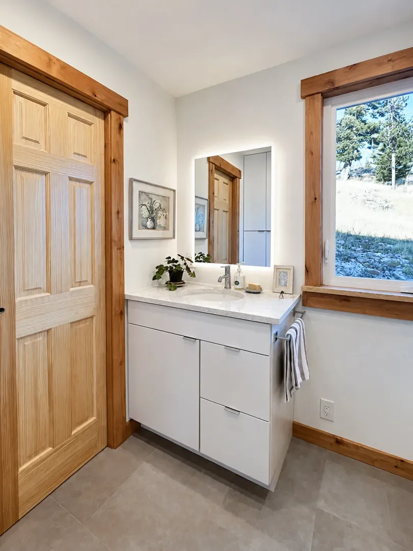 Remodeled rustic contemporary style bathroom in pine brook hills, boulder, co featuring knotty alder pocket doors with wood trim and baseboards, single euro style vanity with LED mirror, and gray ceramic heated tile floor.  