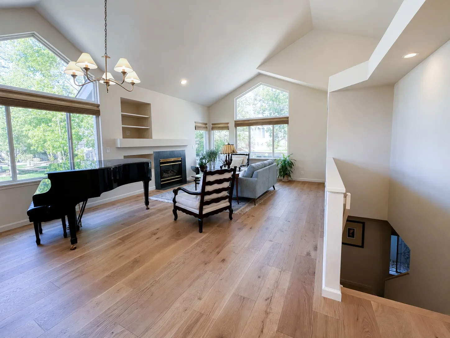 Overview of newly remodeled living room featuring white oak hardwood flooring, blue fireplace tile, vaulted ceilings, and large full height windows with lots of natural light in Gunbarrel, CO