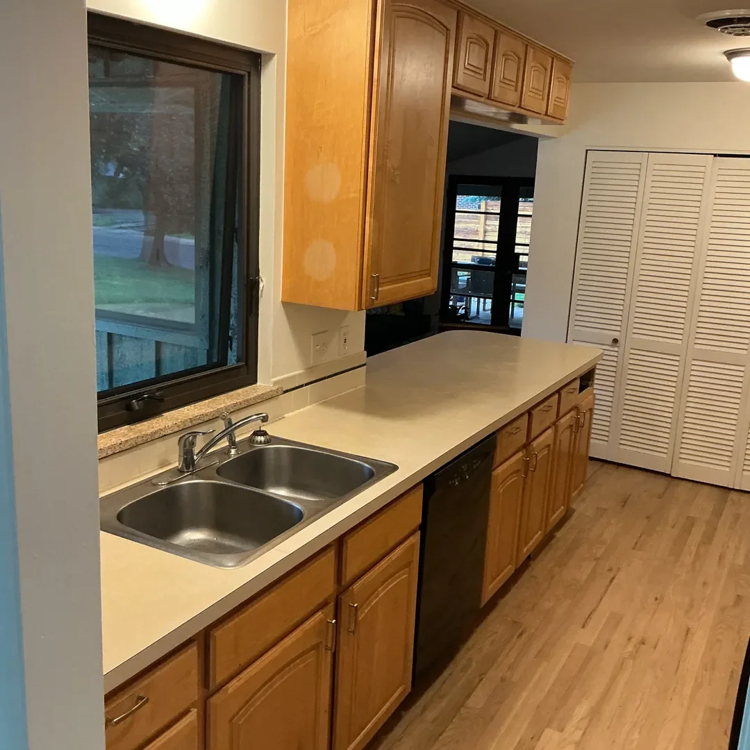 Before photo of kitchen prior to remodeling in Longmont, CO, featuring dated laminate countertops, broken and distressed honey-stained cabinets, and dim lighting