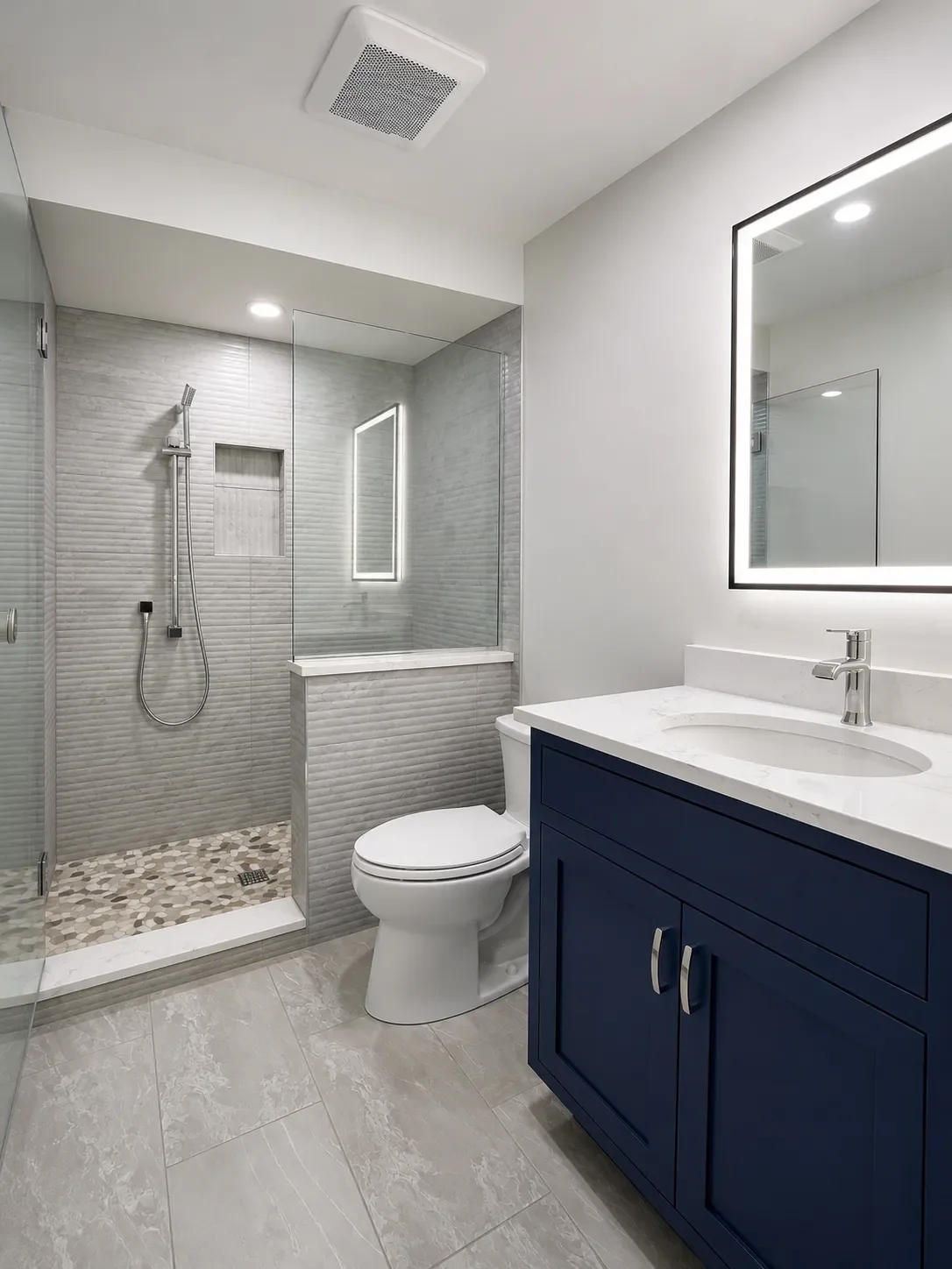 Completed contemporary guest bathroom remodel featuring swinging glass door shower, fluted shower tile, blue vanity, white quartz countertops, and LED mirror in Gunbarrel, CO