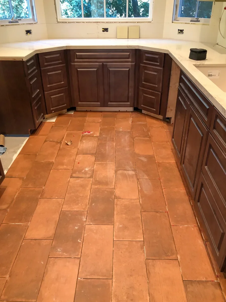Kitchen interior under renovation with unfinished custom cherry wood cabinets, white quartz countertops, and partially finished terracotta tile floor
