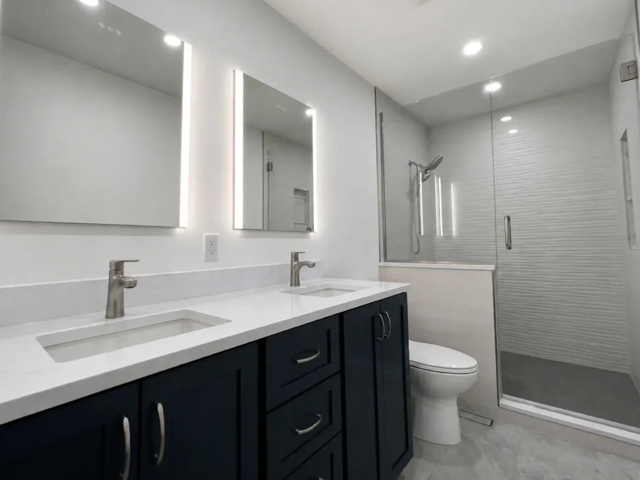 A simple, elegant, contemporary bathroom remodel in Table Mesa, Boulder, CO featuring a frameless glass walk-in shower with textured tile accent wall, blue custom double vanity, LED recessed cabinets, and gray stone tiled floors